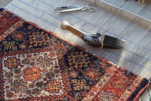 دار قالیبافی با فرش دستباف نیمهتمام، دفتین و قیچی مخصوص قالیبافی در کارگاه سنتی فرش ایران